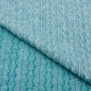 May include: Two pieces of teal blue knitted fabric with different patterns. The top piece has a cable knit pattern and the bottom piece has a chevron pattern.