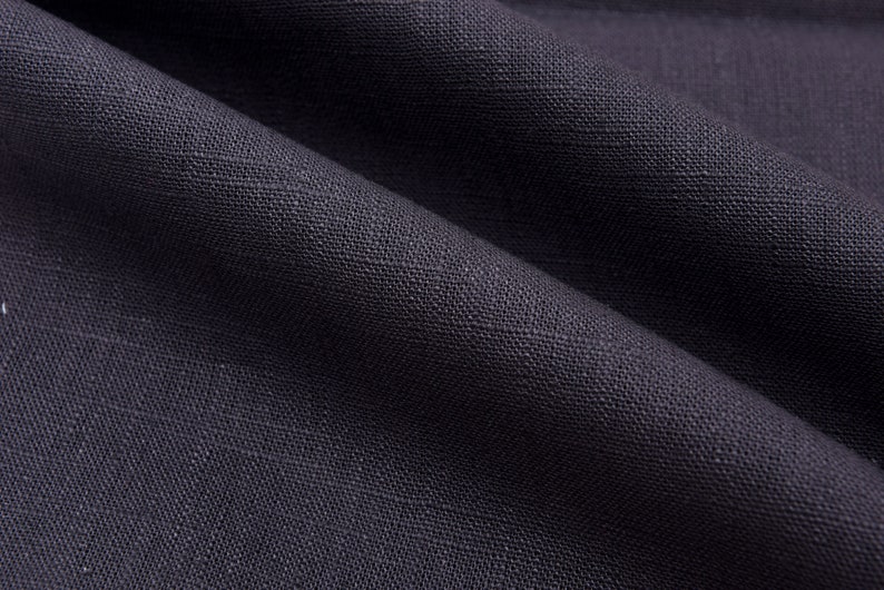 Op de afbeelding: Close-up van een donkergrijze stof met een textuurweefsel. De stof heeft een subtiele glans en een glad, zacht gevoel.