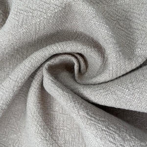 May include: Close-up of a gray linen fabric with a textured weave. The fabric is folded and draped, showing its soft and natural texture.