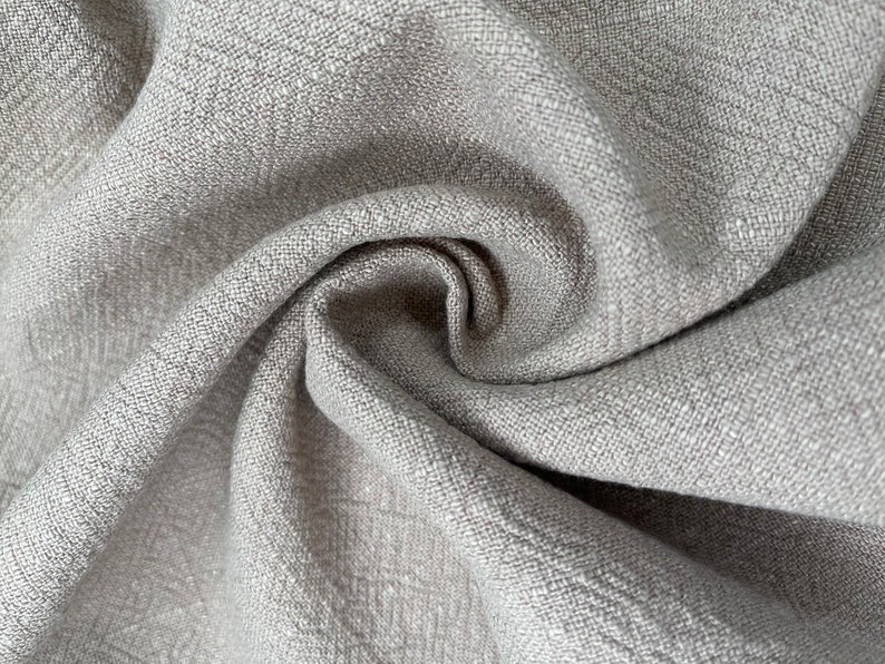 May include: Close-up of a gray linen fabric with a textured weave. The fabric is folded and draped, showing its soft and natural texture.