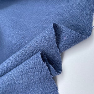 May include: A close-up of a blue fabric with a textured surface. The fabric is folded in half and the edges are slightly frayed.