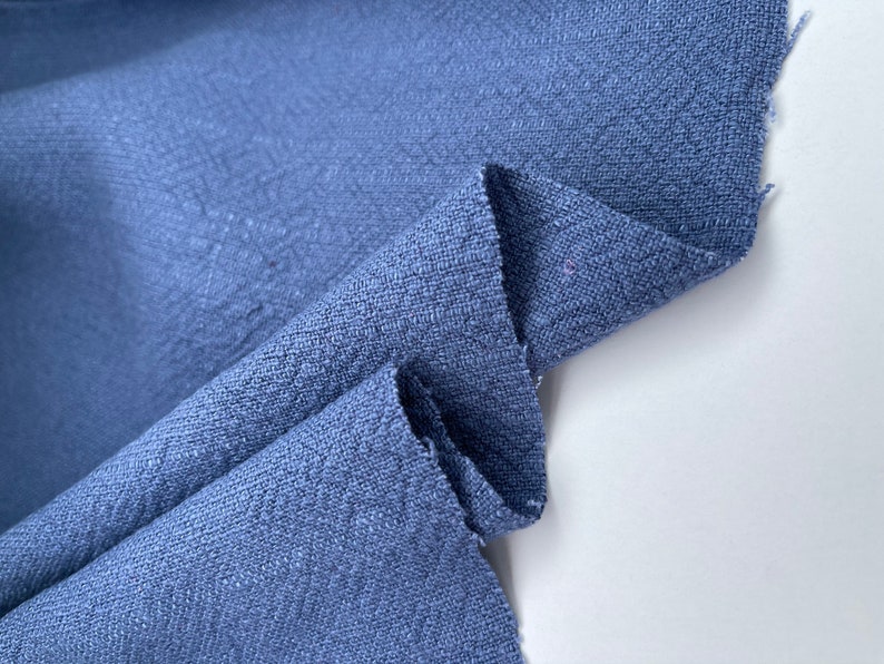 May include: A close-up of a blue fabric with a textured surface. The fabric is folded in half and the edges are slightly frayed.