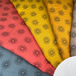 May include: Five fabric swatches with a repeating pattern of black stylized sunbursts on a variety of colored backgrounds, including red, yellow, gray, and brown.