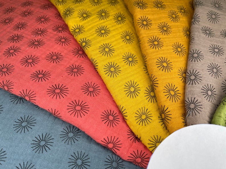 May include: Five fabric swatches with a repeating pattern of black stylized sunbursts on a variety of colored backgrounds, including red, yellow, gray, and brown.