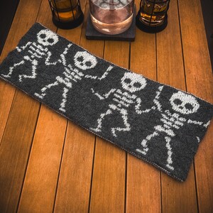 May include: A gray knitted scarf with a white skeleton pattern. The scarf is lying on a wooden surface.