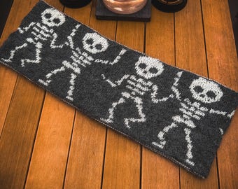 May include: A gray knitted scarf with a white skeleton pattern. The scarf is lying on a wooden surface.