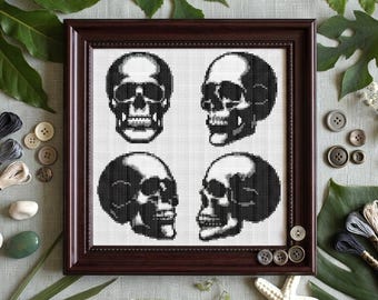 May include: A square cross-stitch embroidery featuring four black and white human skull designs arranged in a grid pattern, encased within a dark brown wooden frame. The skulls are depicted from front, side, and angled perspectives.