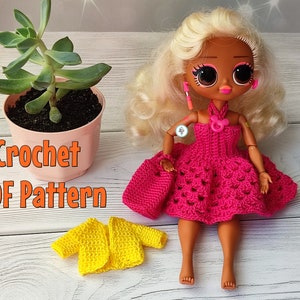 May include: A doll wearing a handmade, hot pink crochet dress, purse, and yellow jacket. The doll has blonde hair and large eyes. A small succulent plant in a pink pot is in the background. The text "Crochet PDF Pattern" is visible.