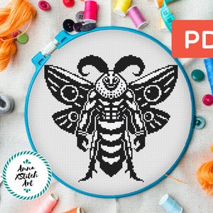 May include: Black and white cross stitch pattern of a moth with large wings and a detailed body. The pattern is displayed in a blue embroidery hoop.