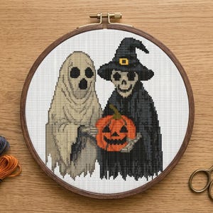 May include: A Halloween-themed cross-stitch design featuring a ghost and a skeleton holding an orange pumpkin. The figures are stitched on white fabric, framed in a wooden hoop. Spools of thread and scissors are visible.
