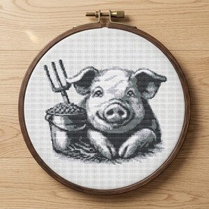 May include: A black and white cross-stitch embroidery of a smiling pig holding a bucket and a pitchfork. The embroidery is set in a wooden hoop, perfect for farmhouse decor. The pig is the central focus of the design.