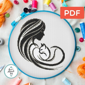 May include: A cross-stitch pattern featuring a woman and a cat in black and white, set in a blue embroidery hoop. The PDF icon is in the upper right. The image is surrounded by sewing supplies, including thread, buttons, and scissors.