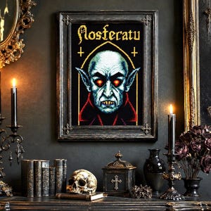 May include: A framed cross-stitch art piece featuring a pixelated portrait of the vampire Nosferatu with glowing red eyes, sharp teeth, and pointed ears. The text Nosferatu is stitched in a gothic font above the figure on a black background.