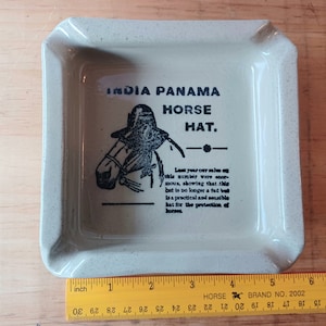 May include: A square, beige ashtray with rounded corners. The ashtray features the text "INDIA PANAMA HORSE HAT" and an illustration of a horse wearing a hat. The text below reads "Last year our sales..."
