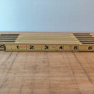 May include: A vintage Craftsman folding ruler, yellow with black markings, showing measurements in inches. The ruler is made of wood and metal, with the numbers 1 through 7 clearly visible. A classic tool for measuring.