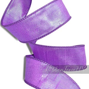 May include: A roll of vibrant purple ribbon with a shimmering, textured surface. The edges are neatly finished with a matching purple stitching. The text "Ribbon Town US" is visible on the ribbon.
