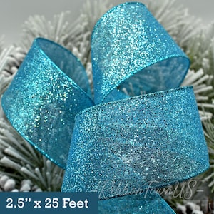 May include: Close-up of a turquoise glitter ribbon. The ribbon is 2.5 inches wide and comes in a 25-foot roll. The ribbon is wrapped in a decorative bow. The background is a blurred image of a frosted evergreen branch.