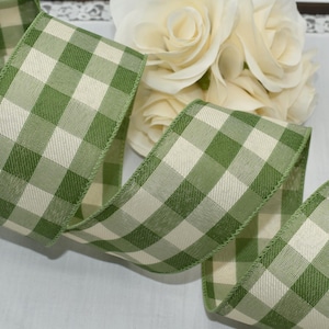 May include: Green and cream gingham ribbon. The ribbon is a wide, decorative style with a classic checkered pattern. The edges are finished with a stitched border. The ribbon is ideal for crafts, gift wrapping, and floral arrangements.