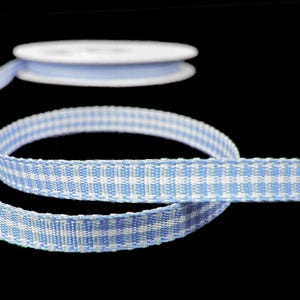 May include: A spool of light blue and white gingham ribbon. The ribbon is woven with a classic check pattern. The ribbon is unspooled, with a portion of the ribbon still on the spool. The background is black.