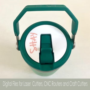 May include: A green travel mug with a white lid and a handle. The lid has a pink inscription that says "Shay".