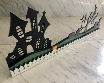 May include: A black and green Halloween countdown calendar with a silhouette of a haunted house and a spooky tree. The numbers 1 through 30 are printed on the calendar.