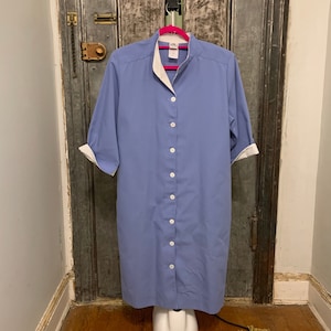 May include: A light blue button-down shirt dress with a white collar and cuffs. The dress has a mandarin collar and is made of a lightweight fabric.