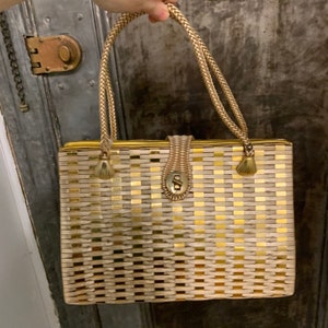 May include: A gold and white woven handbag with a clasp closure and rope handles.