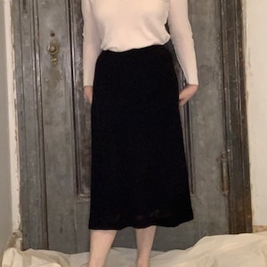 May include: A black midi skirt with a straight silhouette and a slightly flared hem. The skirt is made of a smooth, lightweight fabric.