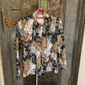 Könnte beinhalten: Eine schwarze Bluse mit floralem Druck, langen Ärmeln und V-Ausschnitt. Die Bluse hat einen Knoten am Hals und ein gerafftes Design.