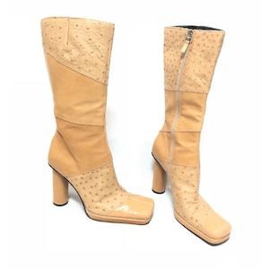 Op de afbeelding: Een paar beige leren laarzen met een vierkante neus en een dikke hak. De laarzen zijn gemaakt van verschillende lederen panelen, waaronder struisvogelprintleer.