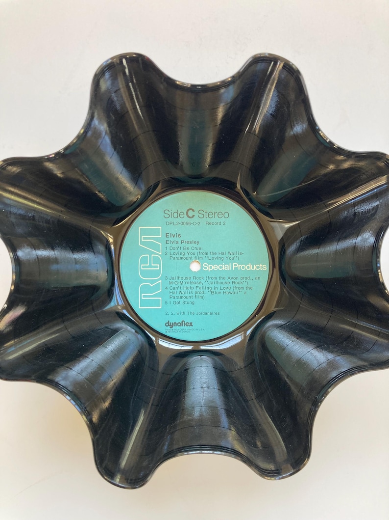 May include: A black, star-shaped bowl made from a recycled vinyl record. The center label is light blue with white text, including "Elvis" and "RCA." The bowl has a unique, wavy edge, and the record's grooves are visible.