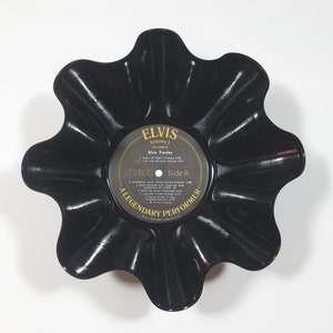 May include: A black, upcycled vinyl record bowl with a scalloped edge. The center label reads "ELVIS Volume 1" and features song titles. The bowl is a unique decorative item, perfect for holding small items or as a display piece.
