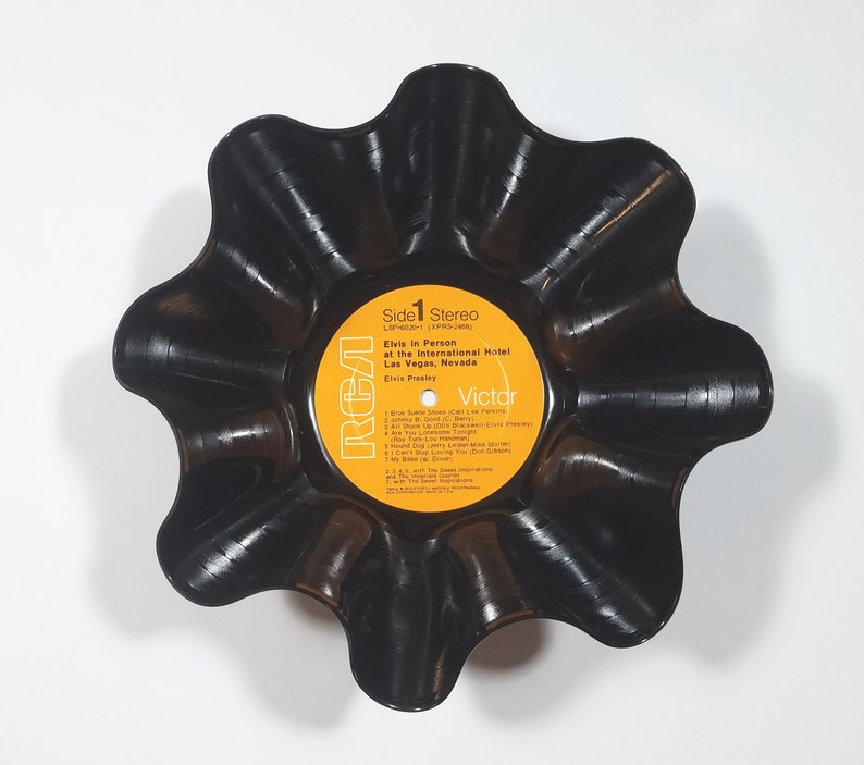 May include: A black, upcycled vinyl record bowl. The bowl is shaped like a flower with wavy edges. The original record label is visible, featuring text that reads "Elvis in Person at the International Hotel Las Vegas, Nevada."