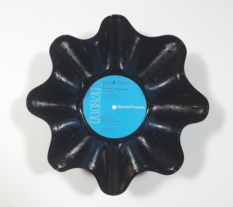May include: A black, star-shaped bowl made from a repurposed vinyl record. The center label is light blue with white text, reading "Side A Stereo" and "Elvis in Hollywood." The RCA logo is visible. A unique decorative piece.