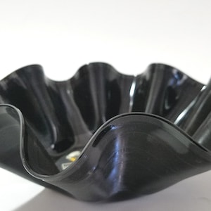 May include: A decorative bowl crafted from a recycled vinyl record. The bowl has a wavy, ruffled edge, and a glossy black finish. The bowl is a unique, eco-friendly home decor item.