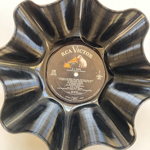 May include: A black, wavy-edged bowl crafted from a recycled vinyl record. The center label features the RCA Victor logo with a dog and a gramophone, and the text "G.I. Blues". The bowl has a unique, handcrafted appearance.