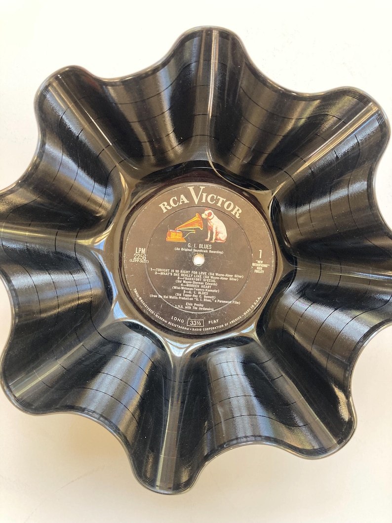 May include: A black, wavy-edged bowl crafted from a recycled vinyl record. The center label features the RCA Victor logo with a dog and a gramophone, and the text "G.I. Blues". The bowl has a unique, handcrafted appearance.