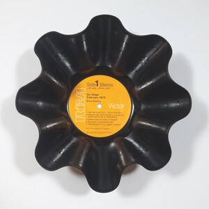 May include: A black, upcycled vinyl record bowl with a scalloped edge. The record label is visible, featuring text including "On Stage February 1970" and "Elvis Presley". The label is yellow with black text and the RCA Victor logo.