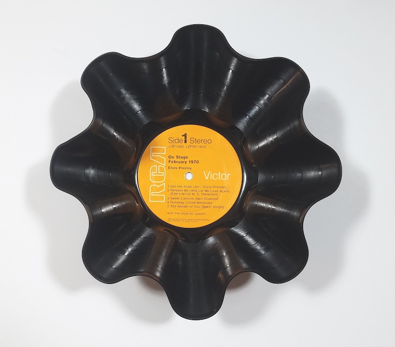 May include: A black, upcycled vinyl record bowl with a scalloped edge. The record label is visible, featuring text including "On Stage February 1970" and "Elvis Presley". The label is yellow with black text and the RCA Victor logo.