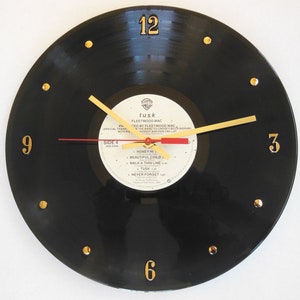 May include: A black vinyl record clock with gold numbers and hands. The record is a Fleetwood Mac album titled "Tusk".