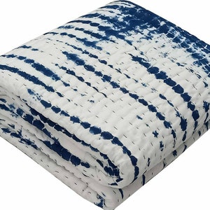 May include: Folded white and blue tie-dye quilt. The quilt features a repeating pattern of dark blue horizontal stripes against a white background. The quilt is stitched with white thread, and the edges are neatly finished.