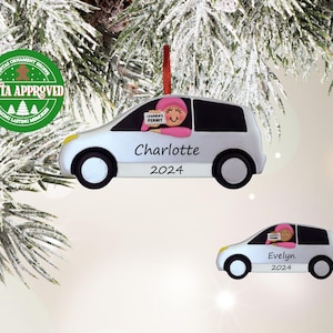 May include: Two white car ornaments with a person inside. The top ornament says "Charlotte 2024" and the bottom ornament says "Evelyn 2024".