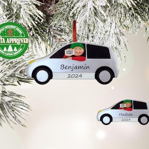 May include: White car ornament with a cartoon driver holding a learner's permit. The ornament is personalized with the name "Benjamin" and the year "2024". A second ornament shows a similar car with the name "Hudson" and the year "2024".