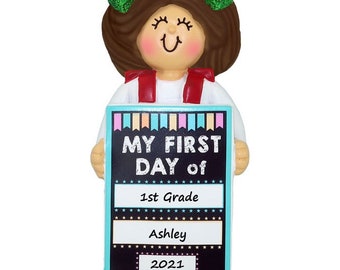 Könnte beinhalten: Ein personalisierter Anhänger mit einem Mädchen mit braunen Haaren und einer grünen Schleife, das ein Schild mit der Aufschrift "My First Day of 1st Grade Ashley 2021" hält.