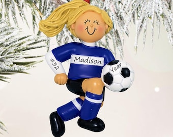 May include: A soccer player ornament with blonde hair in a ponytail, wearing a blue and white jersey with the name Madison and number 32, black shorts, and blue socks. The figure holds a black and white soccer ball labeled with the word Year.
