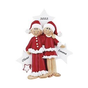 May include: A Christmas ornament featuring two figures in red and white Santa outfits standing together. The ornament includes three white stars with the text 2022, Oliver, and Emma printed on them. The figures have smiling faces and are barefoot.