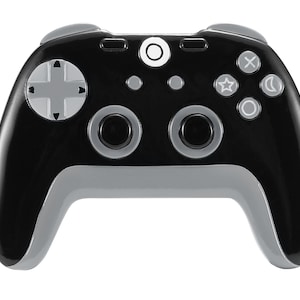 May include: A black and gray video game controller with a circular button in the center and various buttons on the top and sides.