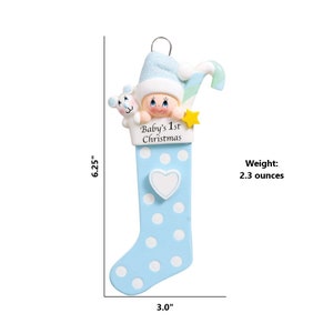 May include: Blue and white Christmas stocking ornament with a baby's face peeking out of the top. The stocking has white polka dots and a white heart on the side. The text "Baby's 1st Christmas" is printed on the stocking. The ornament is 6.25 inches tall and 3 inches wide and weighs 2.3 ounces.