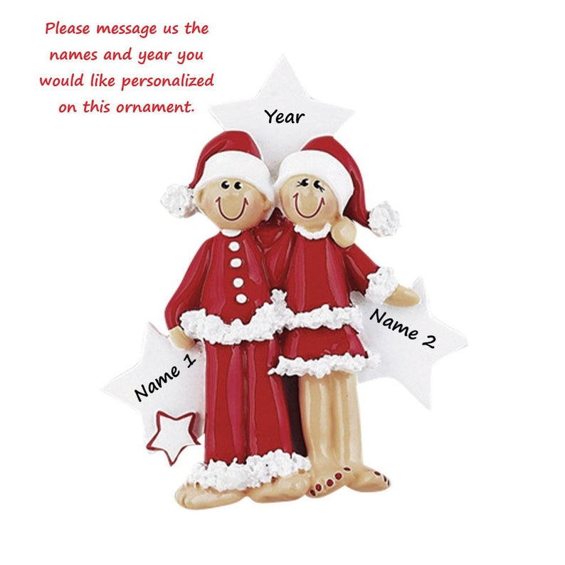 May include: A Christmas ornament featuring two figures wearing red and white Santa suits with matching hats. The figures stand before a large white star labelled Year, with two smaller stars on the sides labelled Name 1 and Name 2 respectively.