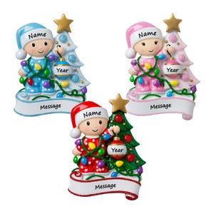 Puede incluir: Tres adornos para &aacute;rbol de Navidad con ni&ntilde;os en pijama y gorros, cada uno junto a un &aacute;rbol decorado. Los adornos incluyen espacios etiquetados como Name, Year y Message. Las figuras presentan temas de colores azul, rosa y rojo.